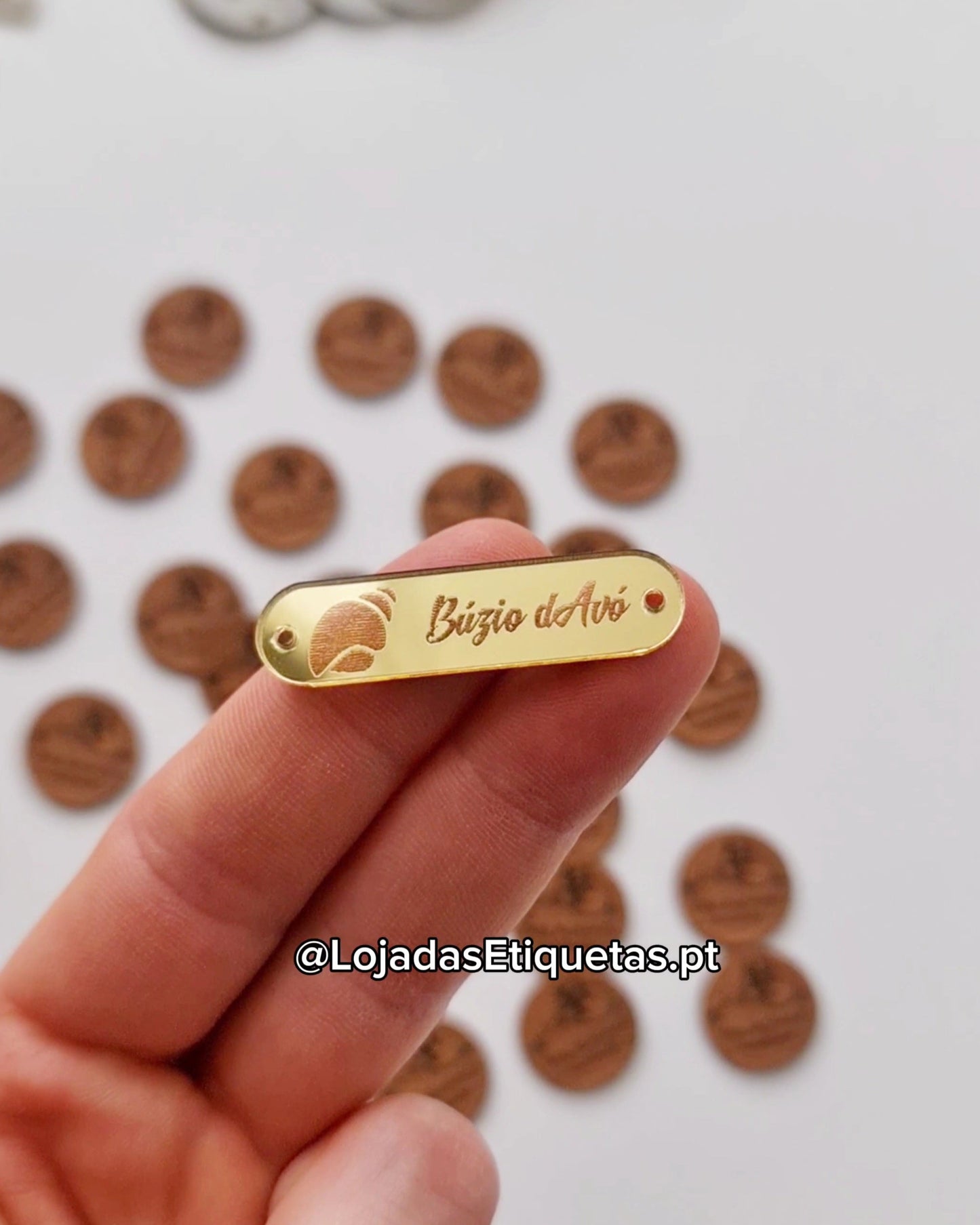 Etiqueta personalizada com logotipo em acrilico dourado. Etiqueta acrílica com cantos arredondados e furos laterais para costura.