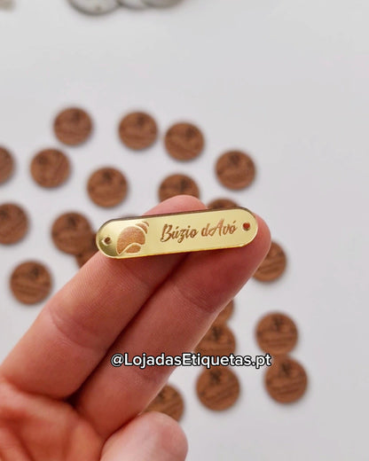 Etiqueta personalizada com logotipo em acrilico dourado. Etiqueta acrílica com cantos arredondados e furos laterais para costura.