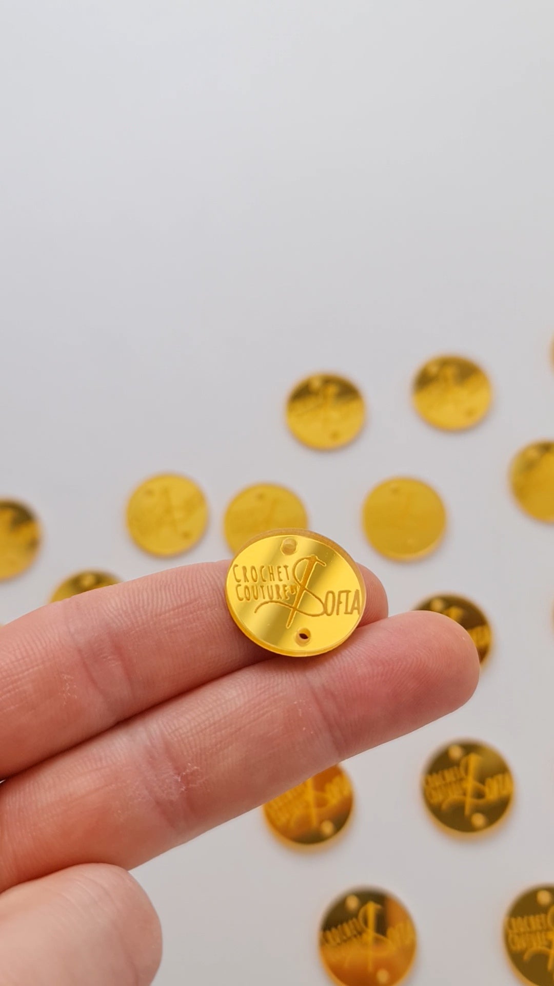 Detalhe de etiqueta redonda com dois furos para costura, personalizada com logotipo. Etiqueta em acrilico dourado espelhado