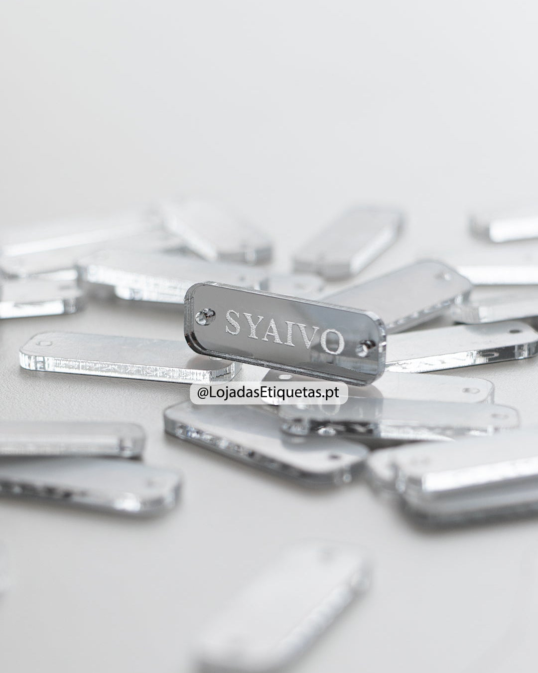 Etiqueta personalizada com logotipo em acrilico espelhado prateado com furos laterais.