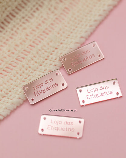 Etiqueta personalizada com logotipo em rosa claro espelhado. Etiquetas retangulares com cantos rectos e etiquetas com cantos arredondados. 4 furos para costura.